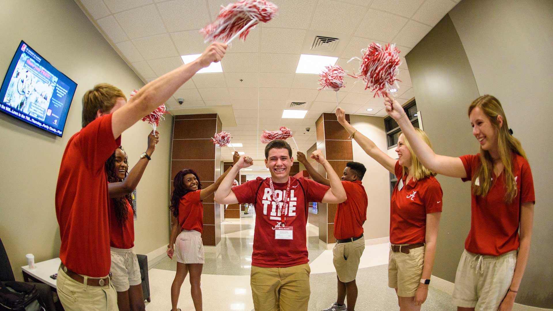 a line of avantis waving pom poms cheer while greeting a male bama bound attendee who smiles holding his fists in the air