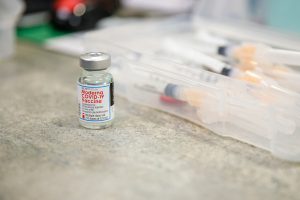 A vial containing a COVID-19 vaccine with syringes behind.