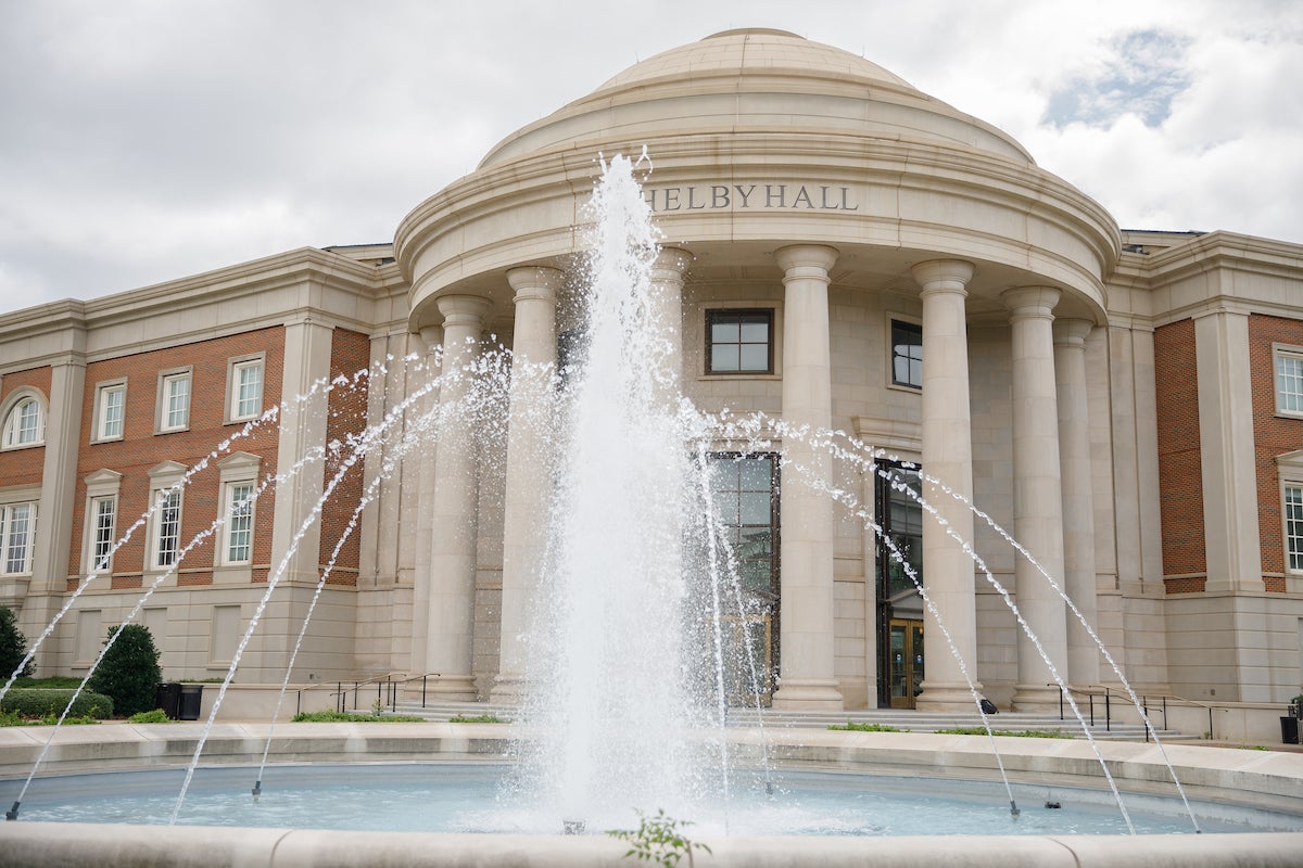 A fountain is spurting out water. The fountain is in front of a building.