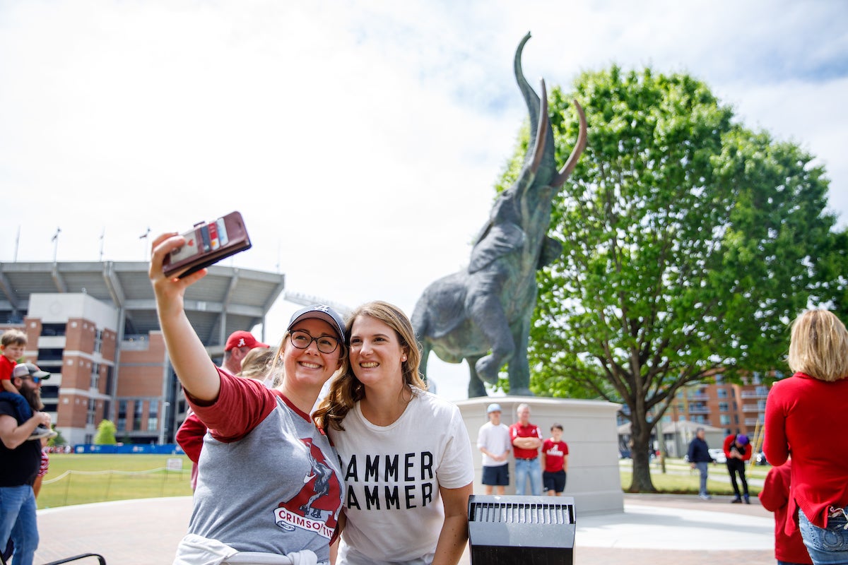 Two girls stand together taking a selfie with the bronze elephant statue, Tuska.