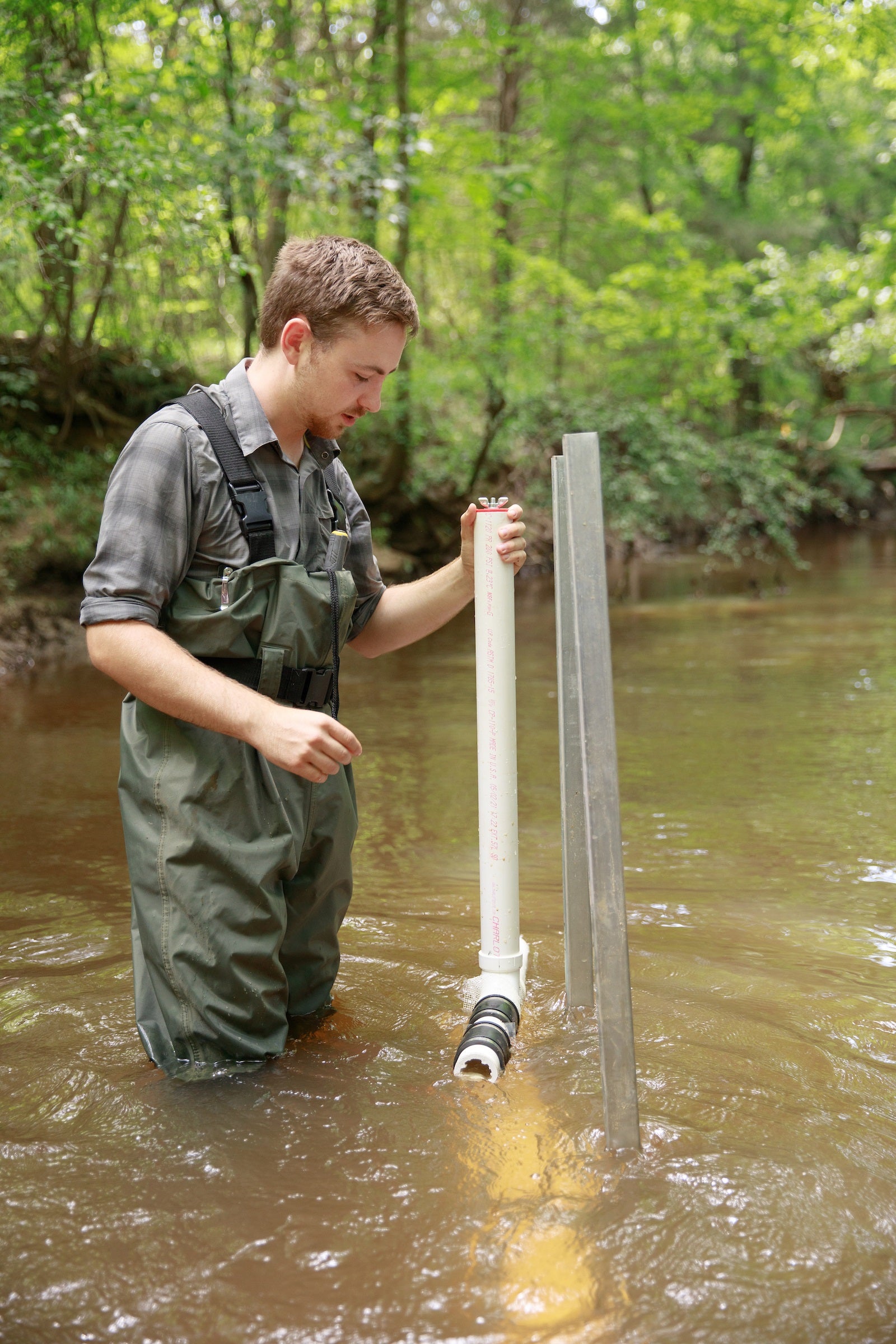 A man in waders works with scientific equipment in a stream.