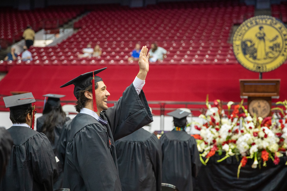 A male student in profile waves his hand in the air to signal someone.