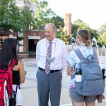 Dr. Bell stands outside taking to two students wearing backpacks during First Day UA