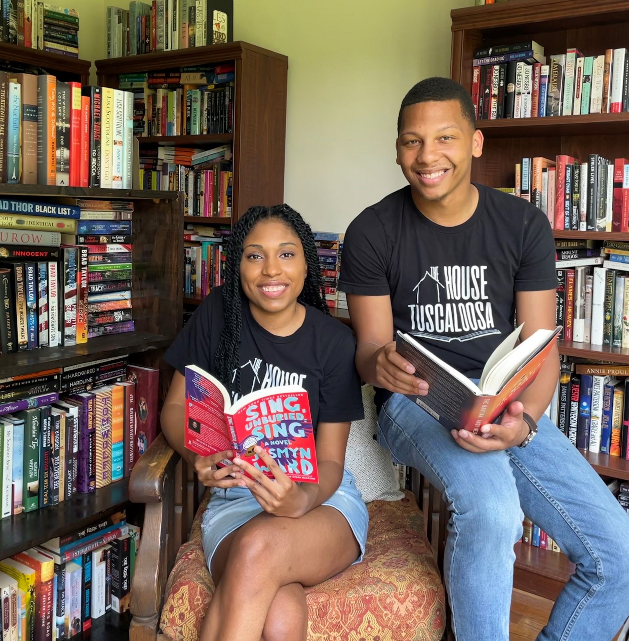 A woman and man post in front of bookshelves while sitting in a chair.