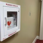 Close up of a white AED box mounted on a wall in the hallway of Rose Administration building
