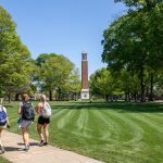 photograph of three students wearing backpacks and walking across the Quad on a clear, sunny day