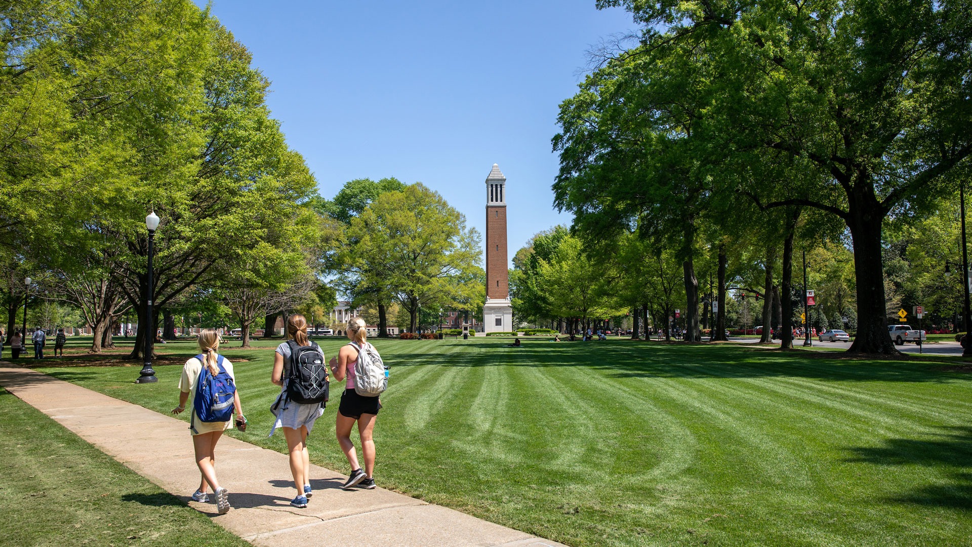 photograph of three students wearing backpacks and walking across the Quad on a clear, sunny day