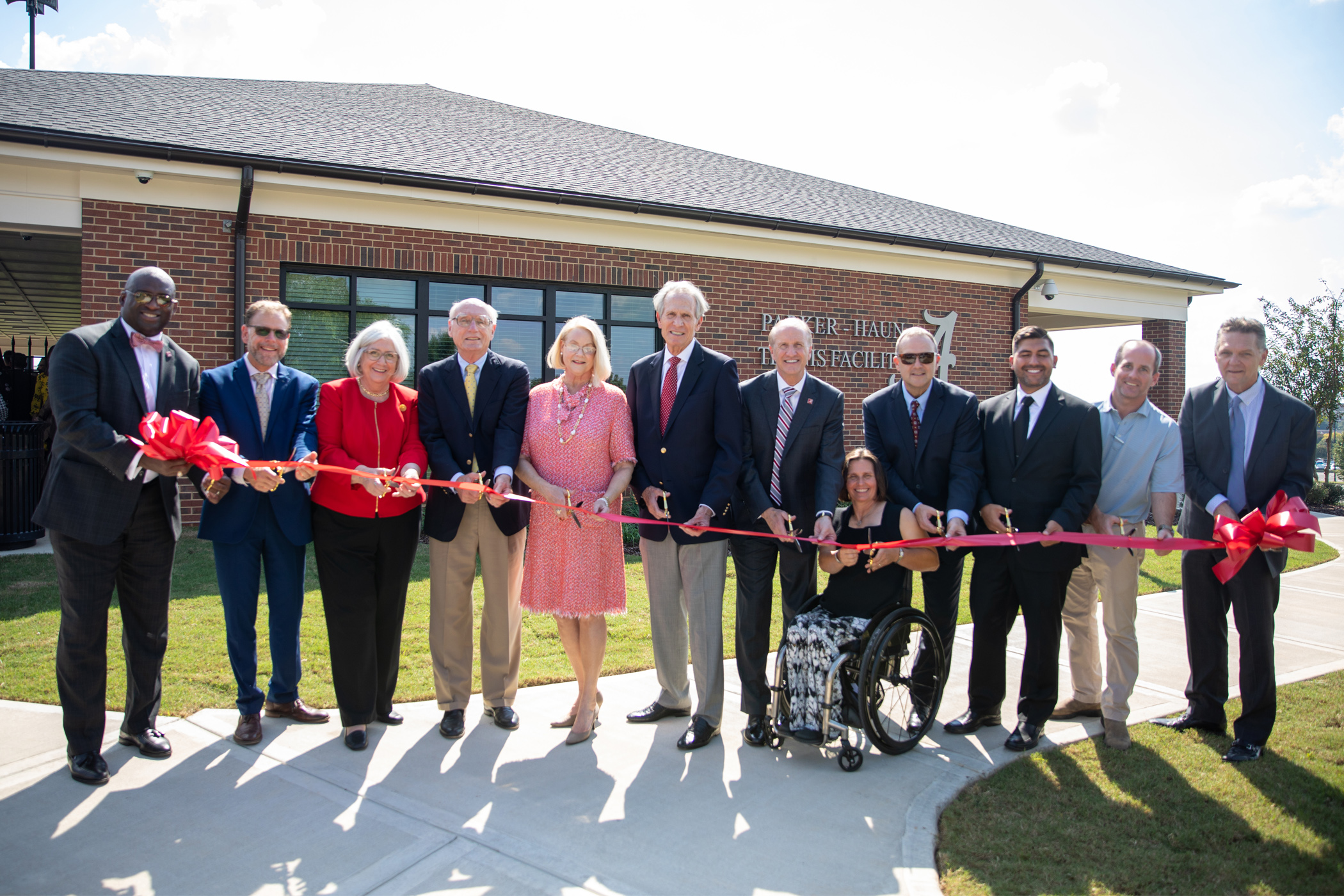 Several university representatives cutting the ribbon in front of the Parker-Haun Tennis Facility