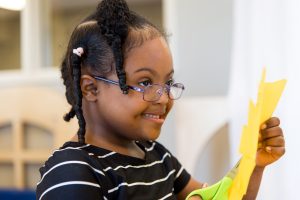 A RISE student smiling while cutting a piece of paper