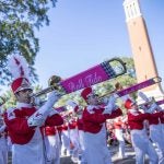 Several people dressed in marching band gear play instruments while in the homecoming parade.