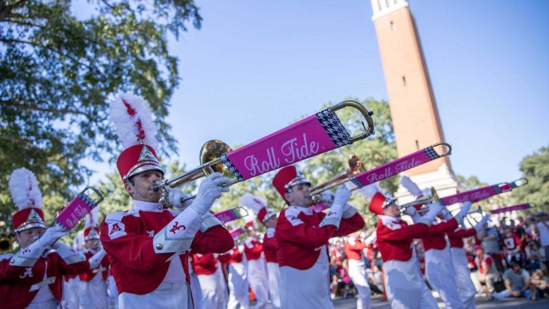 Several people dressed in marching band gear play instruments while in the homecoming parade.