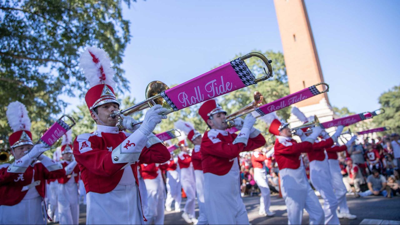Several people dressed in marching band gear play instruments while in the homecoming parade.