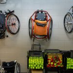 Tennis wheelchairs hanging on the wall and tennis balls in crates in the equipment room