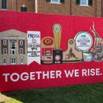 On a red background, the words "Together We Rise" are written out in white. Several UA awards and new monuments are also shown.