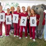a group of nursing students wearing crimson scrubs smile while holding up numbers to denote the 2021 campaign fundraising total of $406,720