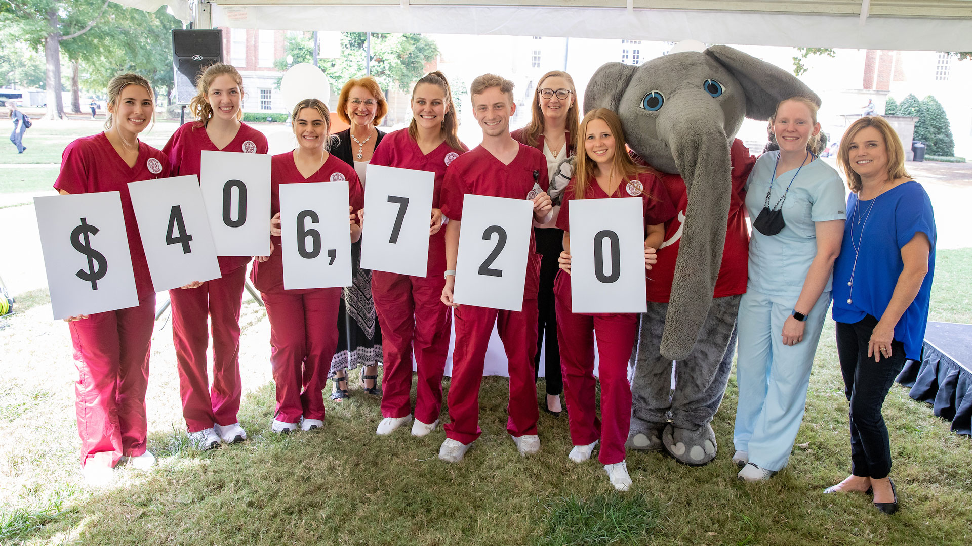 a group of nursing students wearing crimson scrubs smile while holding up numbers to denote the 2021 campaign fundraising total of $406,720