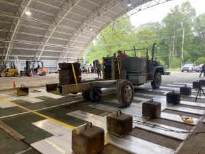 A military truck drives over metal matting as a test inside a hangar.