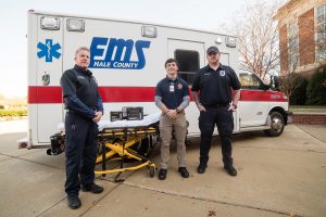 Three paramedics pose in front of an ambulance.
