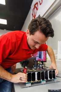 A man in a red shirt works on a piece of technical equipment on a table.