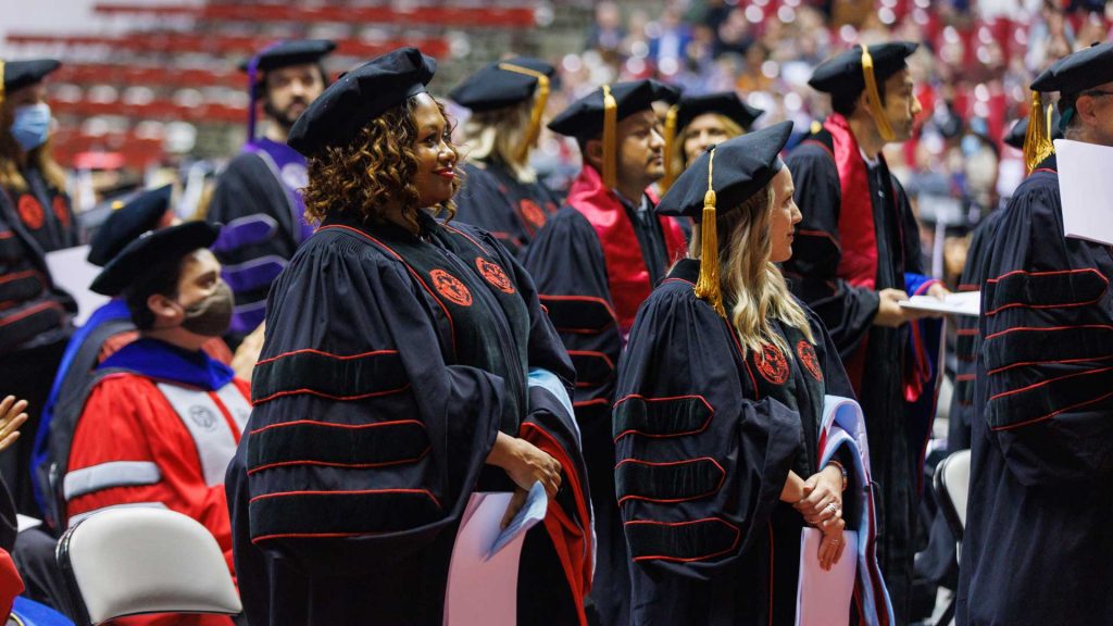 A group of women stand in a crowd dressed in doctoral robes.