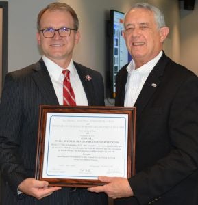 Two men in suits smile while holding a certificate.