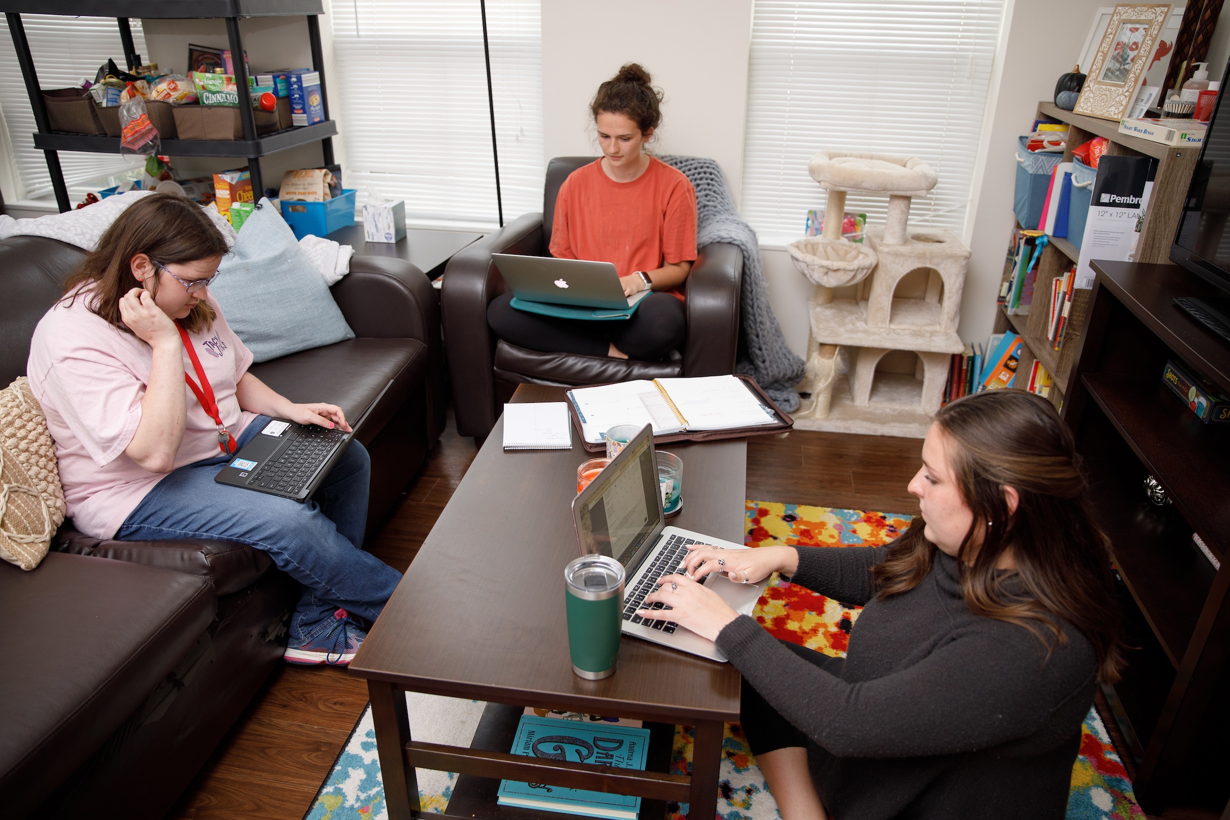 Four women sit in a living room while studying on laptops.