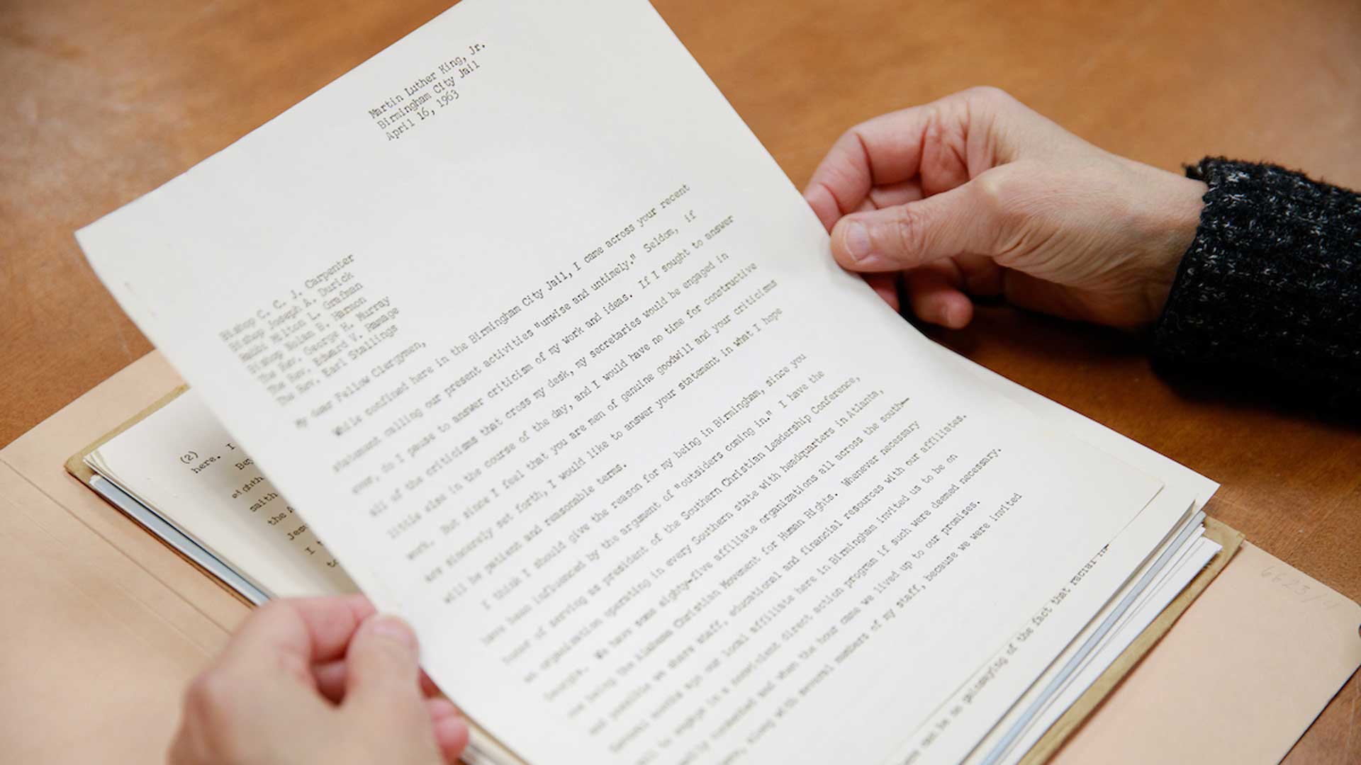 On a natural grain background, two hands can be see holding up a copy of a letter written by Martin Luther King Jr. in 1963.