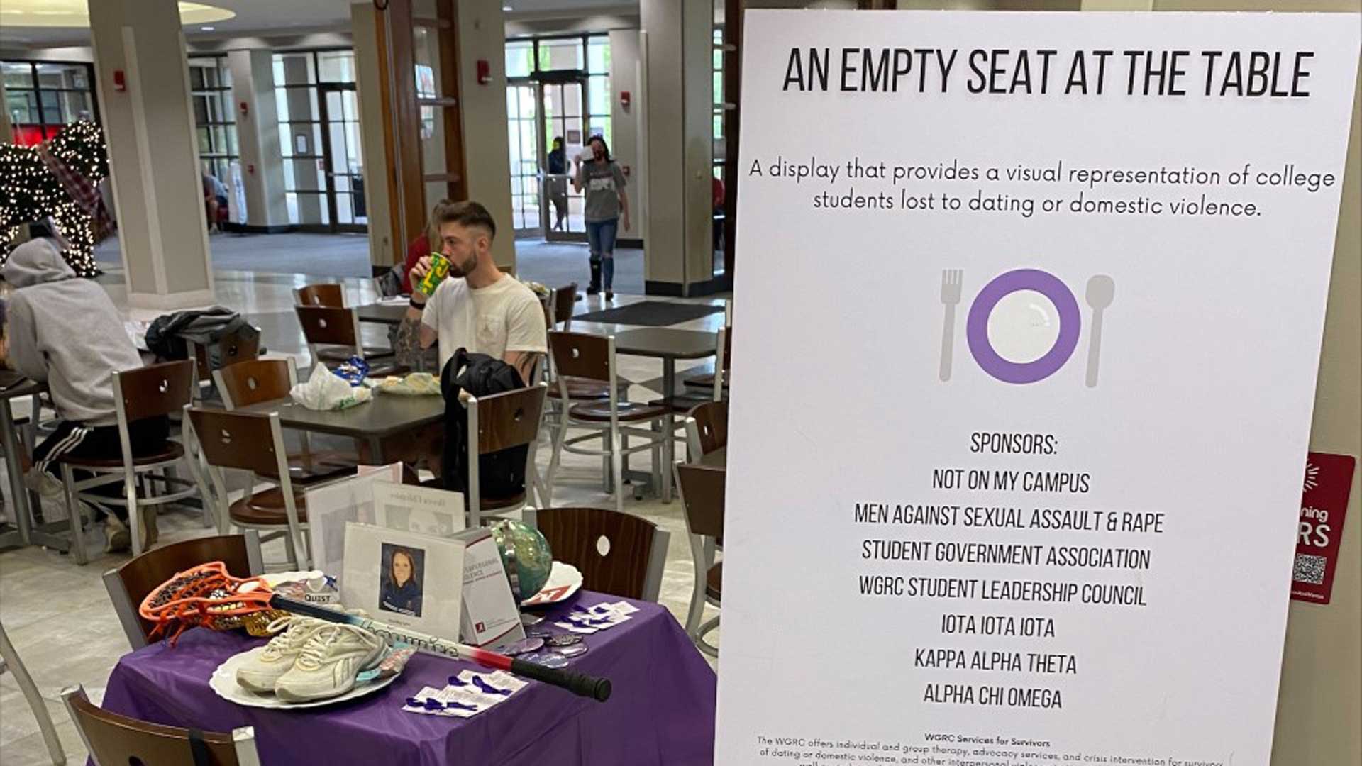 an empty table with a purple tablecloth set up in a dining hall to raise awareness about domestic violence
