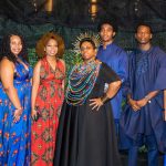 Eight people pose together in traditional African attire.