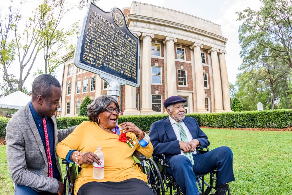 Dr. foster and her husband sitting in wheelchairs next to the historical marker
