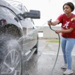 A Black female uses a hose to wash off a tire.