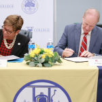 Cynthia Warrick and Stuart R. Bell sit at a table signing documents.