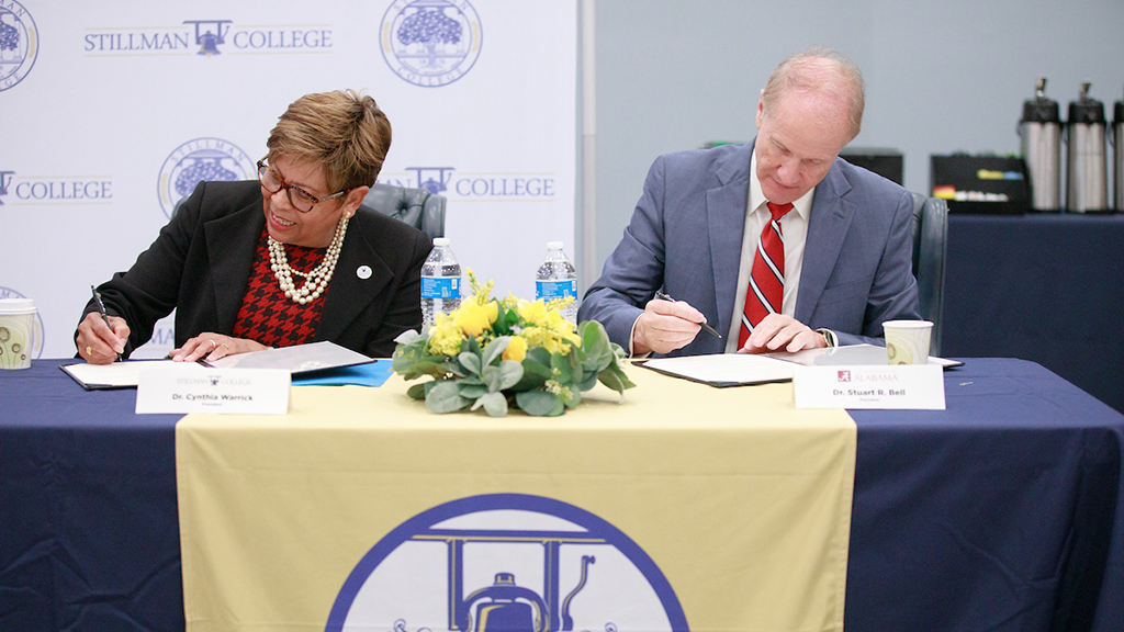 Cynthia Warrick and Stuart R. Bell sit at a table signing documents.