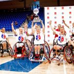 The women's wheelchair basketball team celebrates their victory on the court by raising the trophy