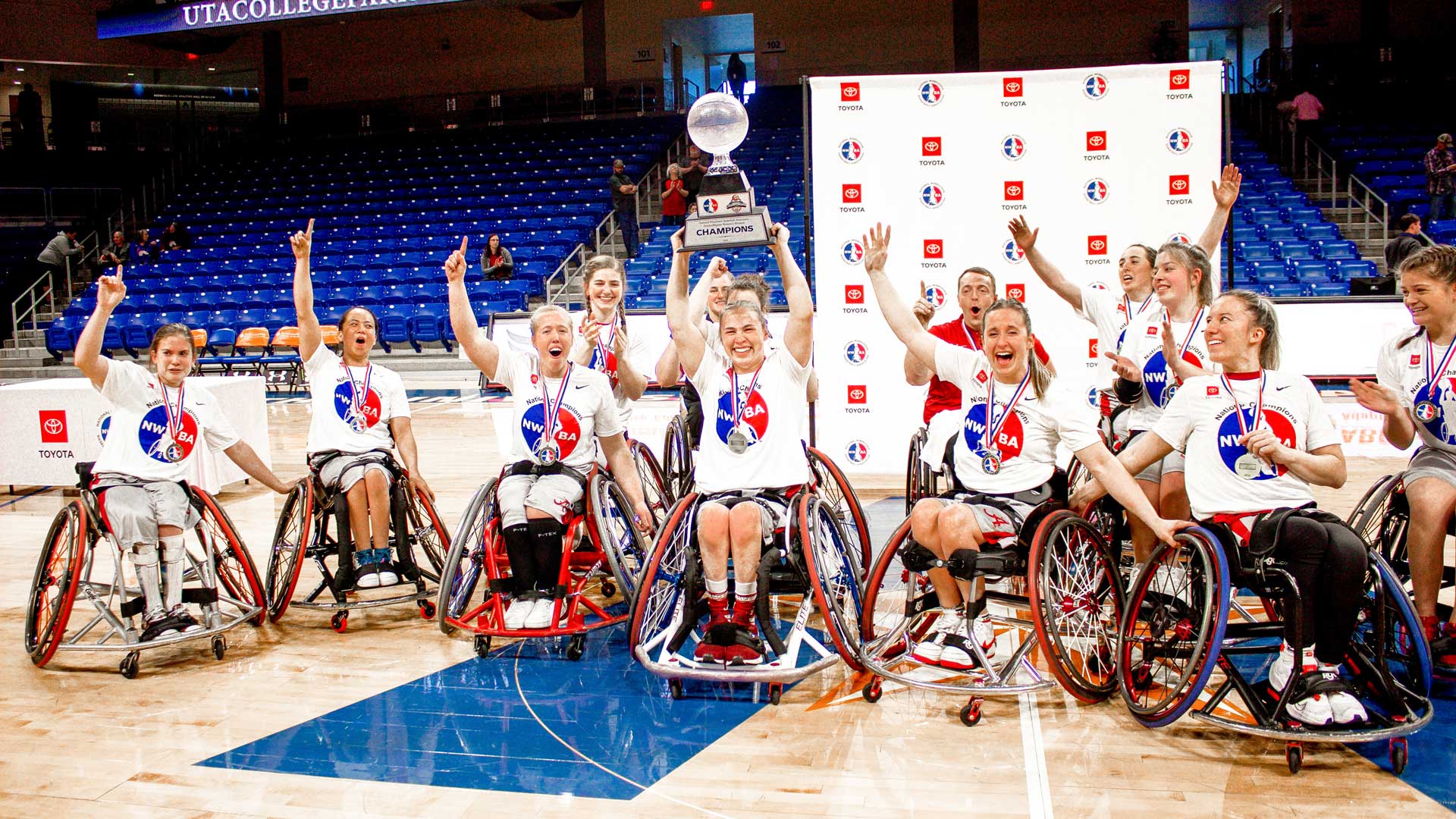 The women's wheelchair basketball team celebrates their victory on the court by raising the trophy