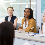 women talk while sitting at a board room table