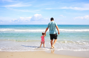 A father and daughter walking on a beach.