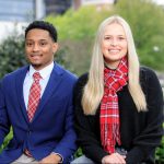 Two students sit outside Bryant Denny stadium wearing the UA tartan