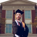 Mason Aldridge in cap and gown in front of the capstone college of nursing building