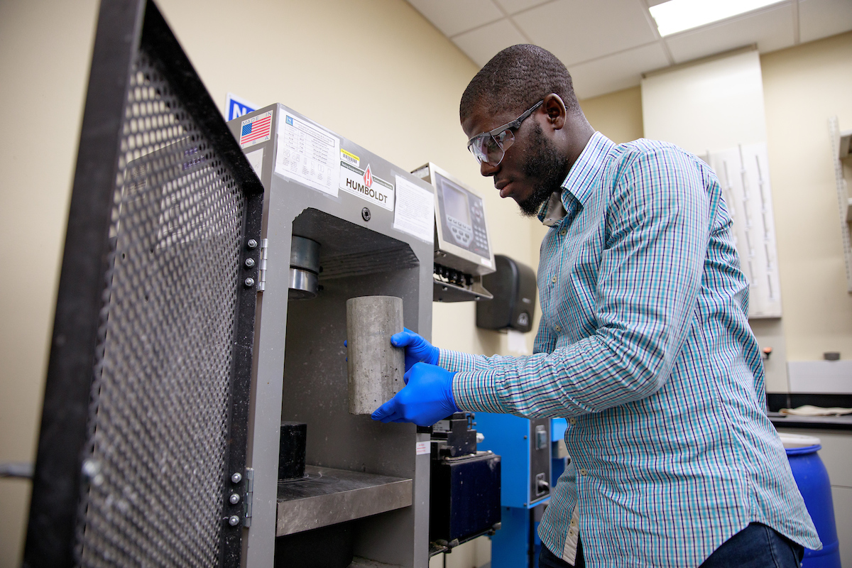 An engineering graduate student at The University of Alabama places cylindrical samples of concrete into a machine.