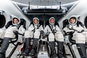 Four people in spacesuits sit inside the space capsule.