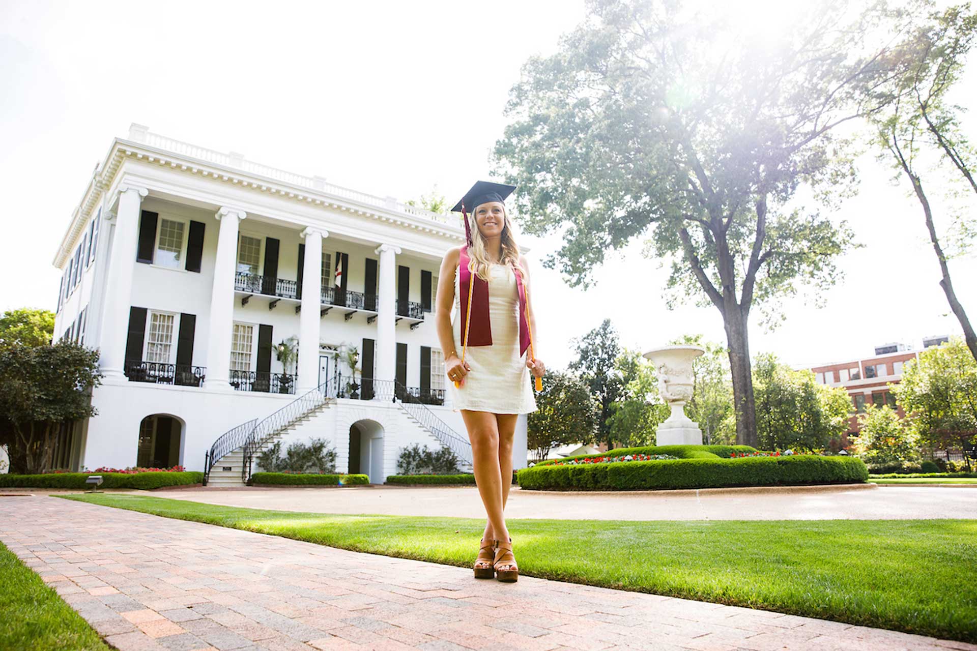 student wearing graduation cap standing in front of the president's mansion