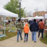 the backs of a group of people walking among tents of art vendors at the 2018 Druid City Arts Festival