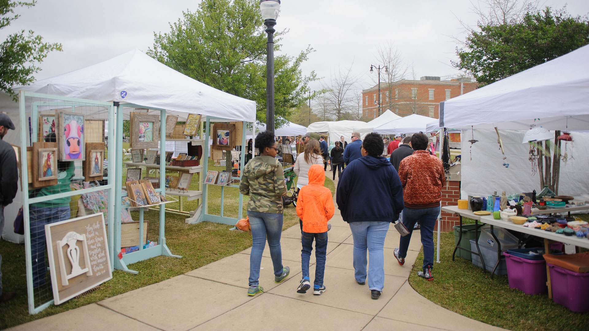 the backs of a group of people walking among tents of art vendors at the 2018 Druid City Arts Festival