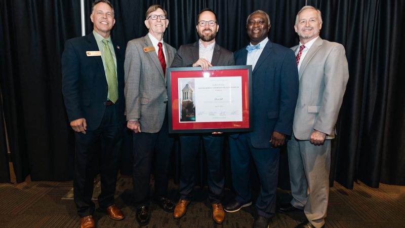 Chris Gill is pictured with university leadership while holding his award