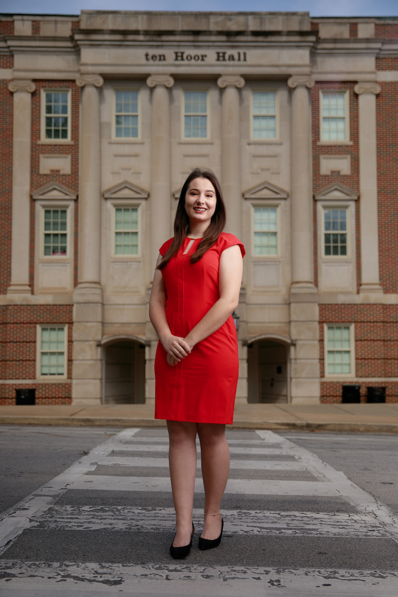 A University of Alabama graduate poses in a dress in front of a classroom building.