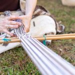A woman is making a textile using traditional Native American tools.