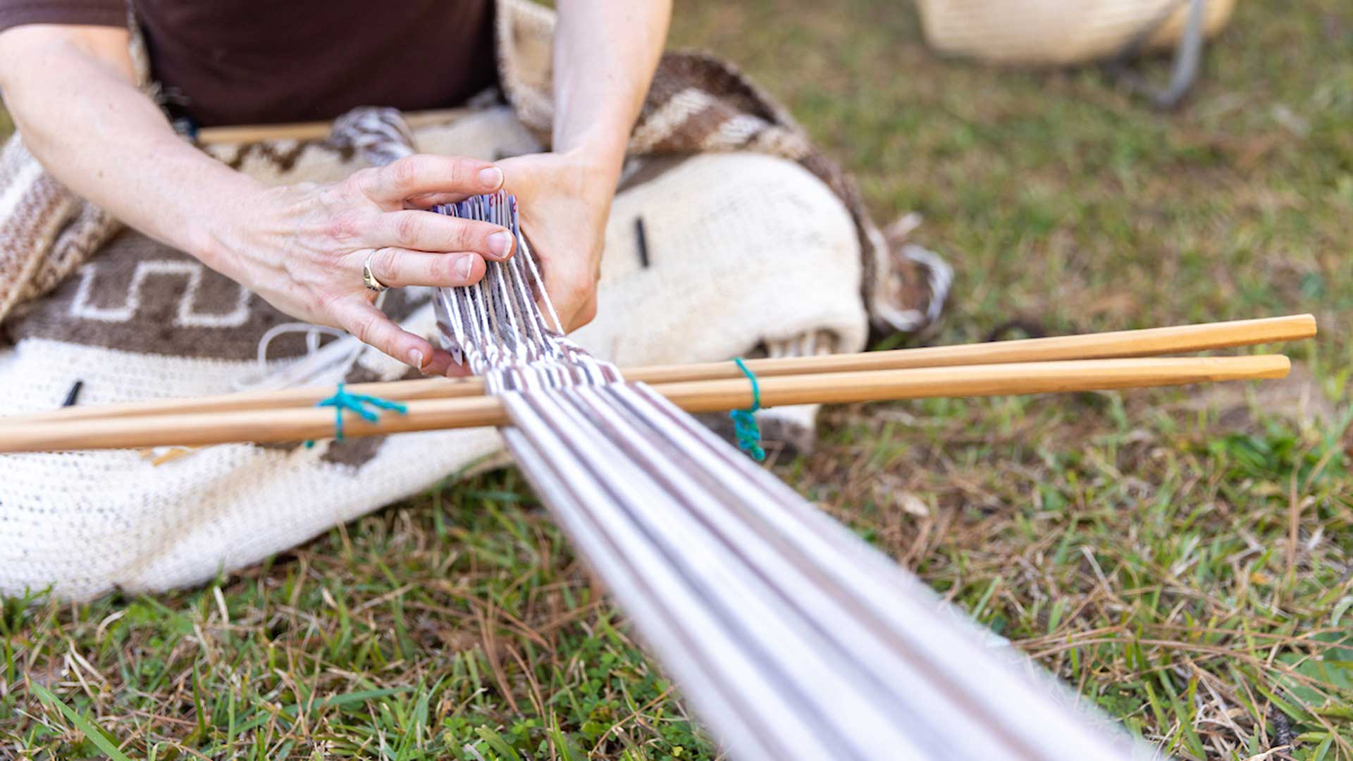 A woman is making a textile using traditional Native American tools.