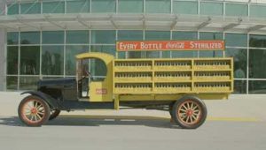 A vintage yellow Coca-Cola truck is parked on a street.