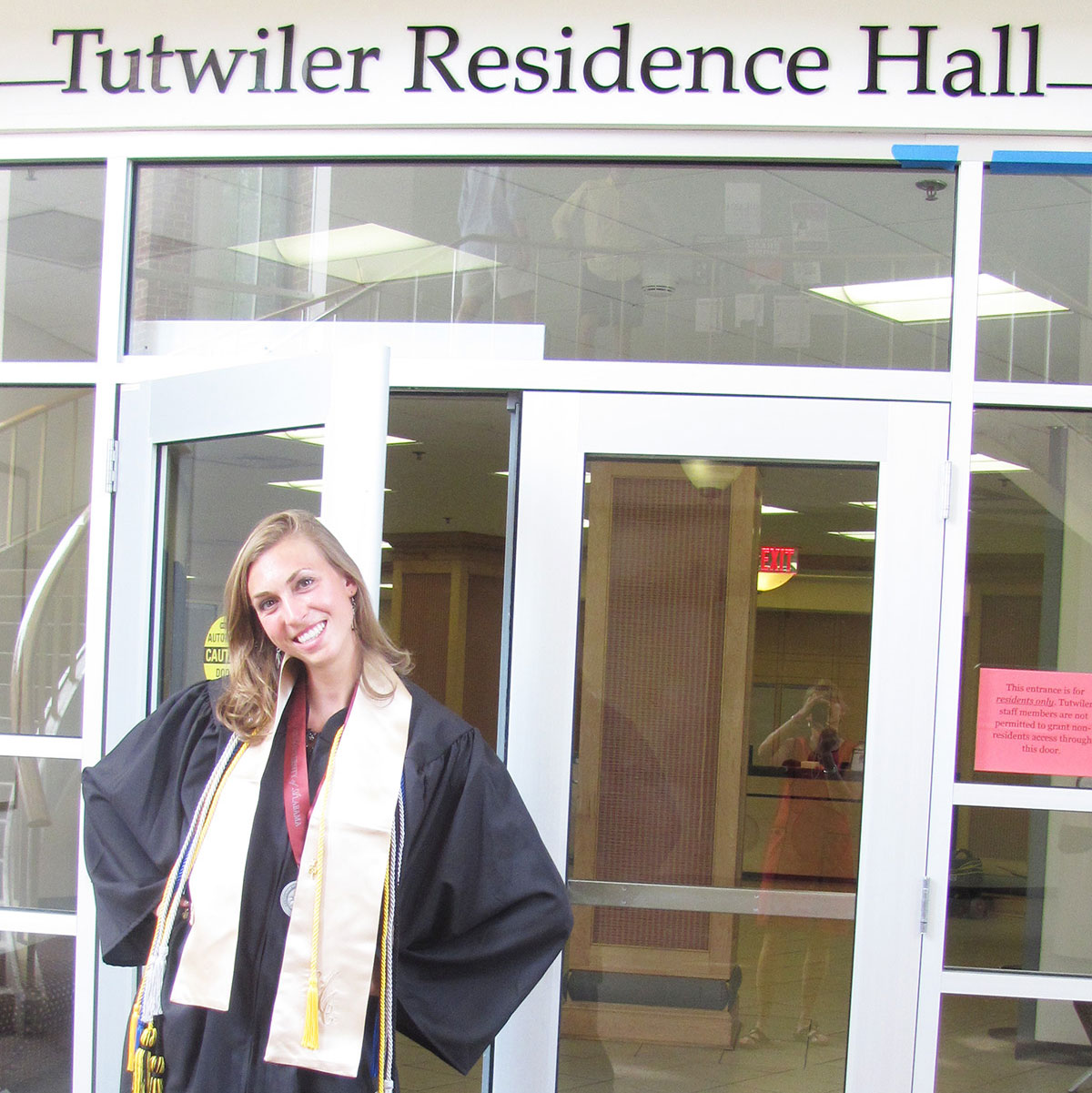 Emily Wolf wearing a graduation robe and stoles stands in front of the entrance to Tutwiler Hall